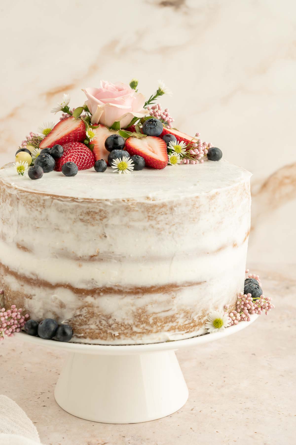 A slice of vegan sponge cake on a white plate, showing the fluffy interior and vanilla frosting between layers.