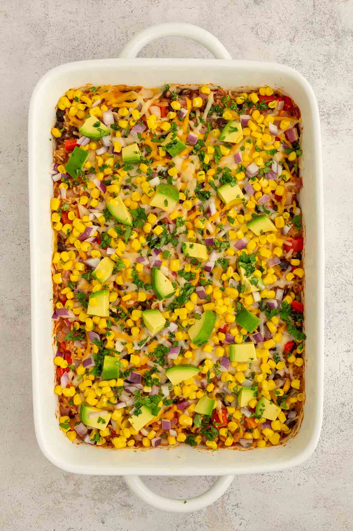 Bean and rice casserole with lots of toppings including red onion, cilantro, and corn kernels.
