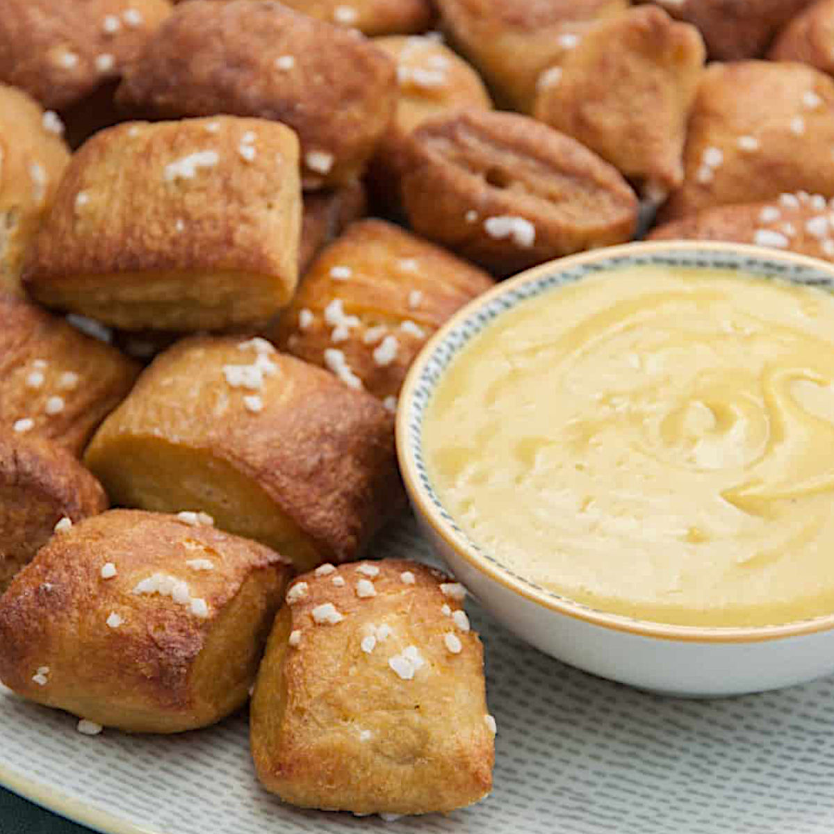 A pile of vegan pretzel bites on a plate with a bowl of vegan cheese dip.