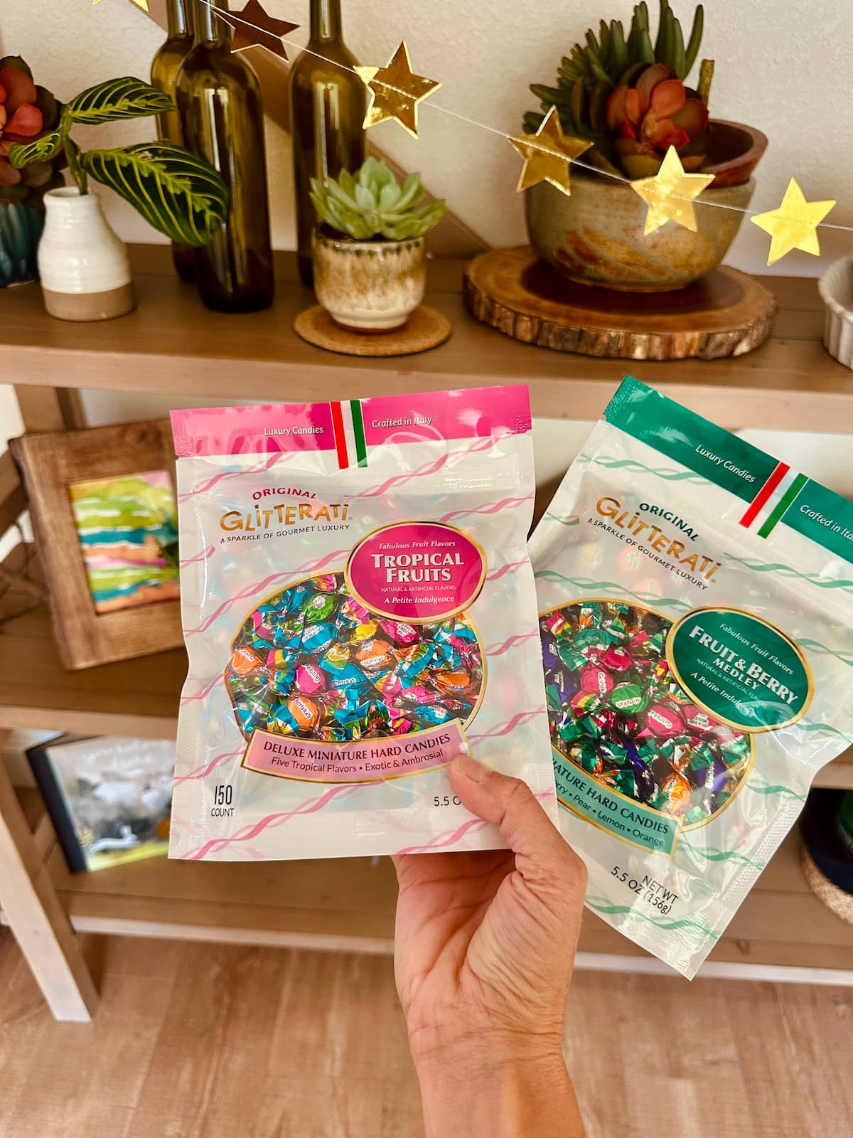 A hand holding two packages of Glitterati hard candies made in Italy. Shown in Fruit & Berry and Tropical Fruits flavors.