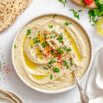 Roasted eggplant in a bowl served with a spoon and topped with a drizzle of oil and fresh chopped herbs.