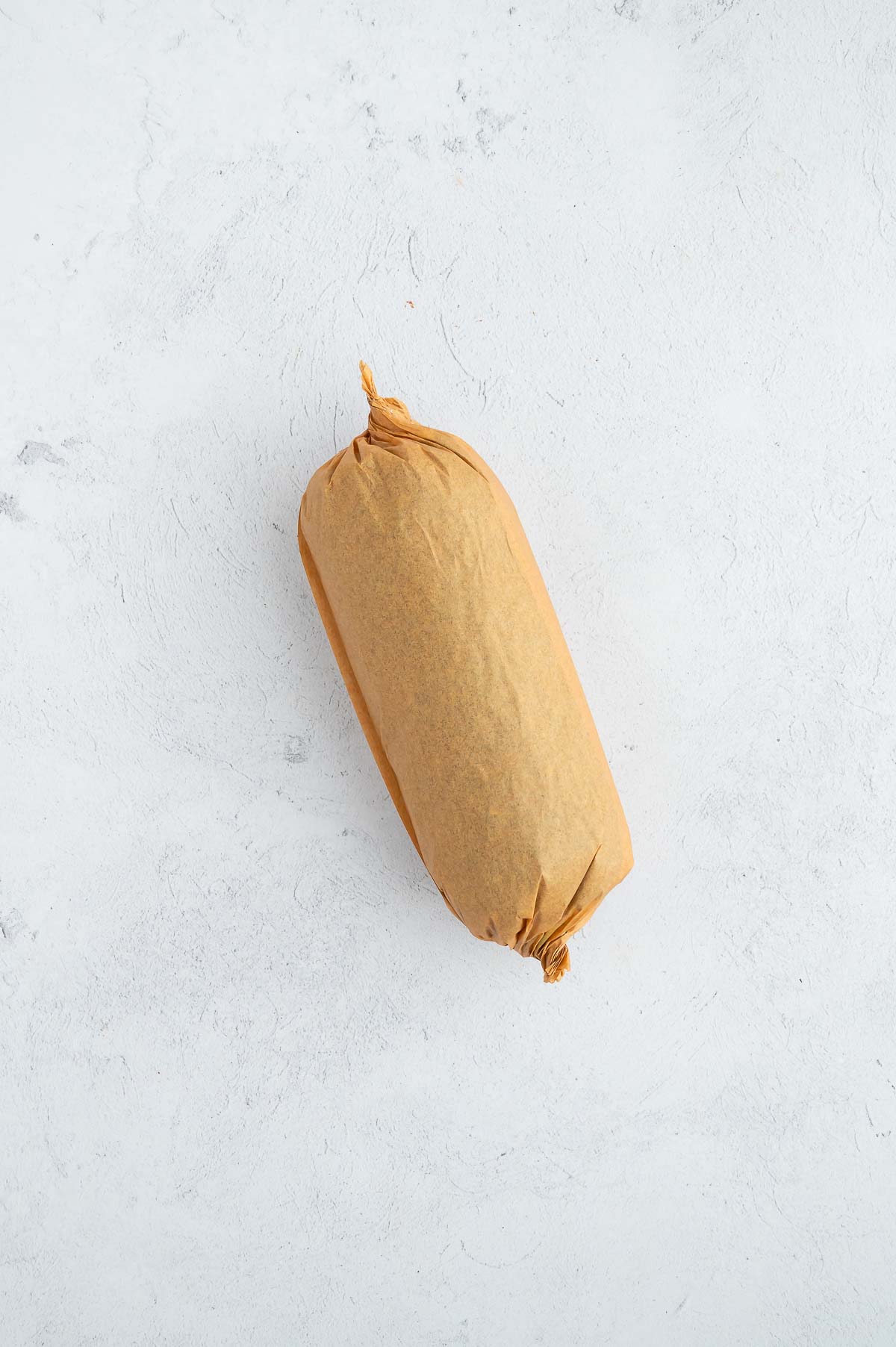 Fully wrapped sushi burrito secured in parchment paper with twisted ends, ready to slice or store.