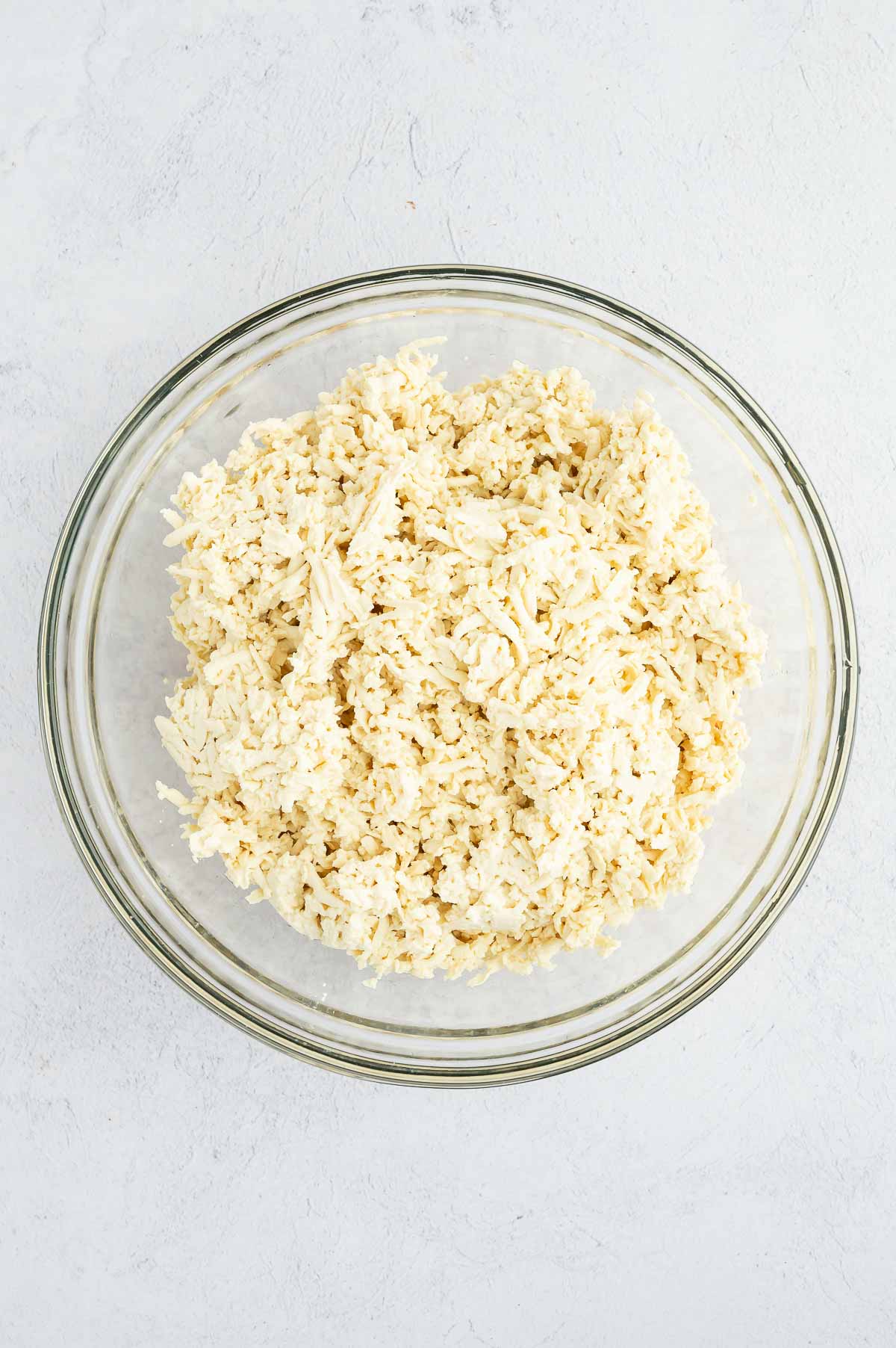 Glass bowl filled with freshly shredded tofu, prepped and ready to be seasoned for the sushi burrito filling.