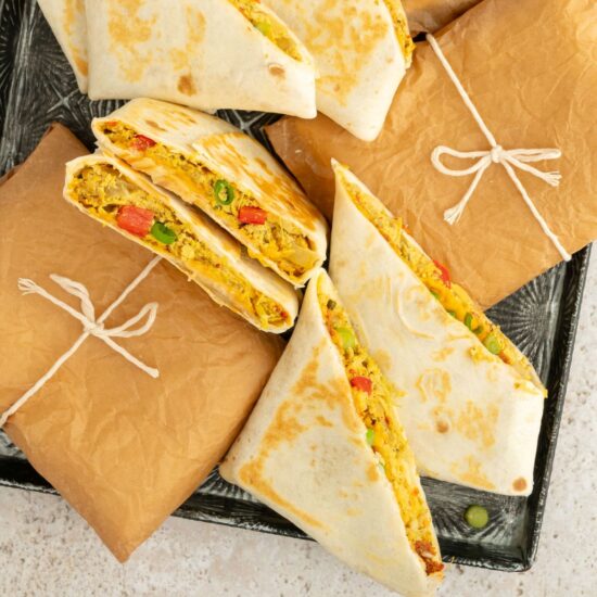 A tray of vegan breakfast burritos with some sliced in half to show the filling.