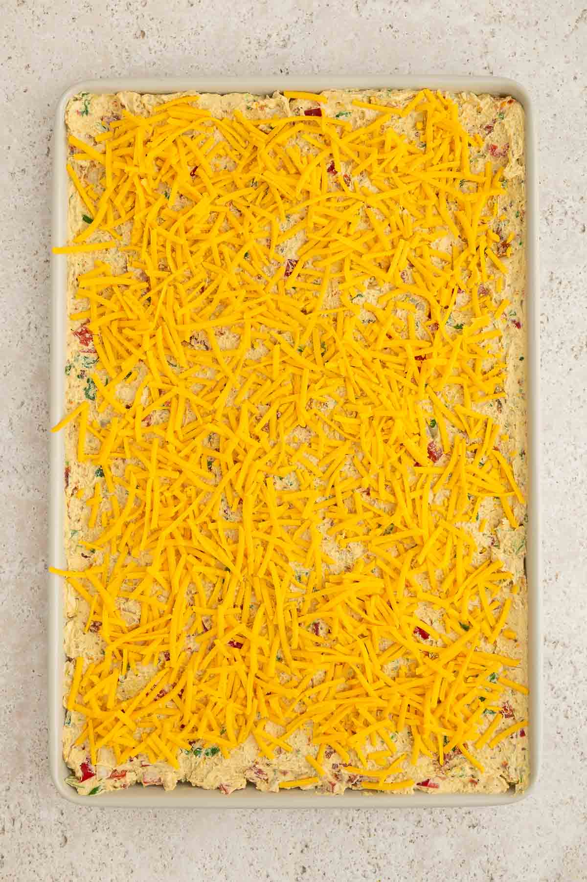 The vegan burrito filling spread evenly on a sheet pan and topped with vegan shredded cheese.