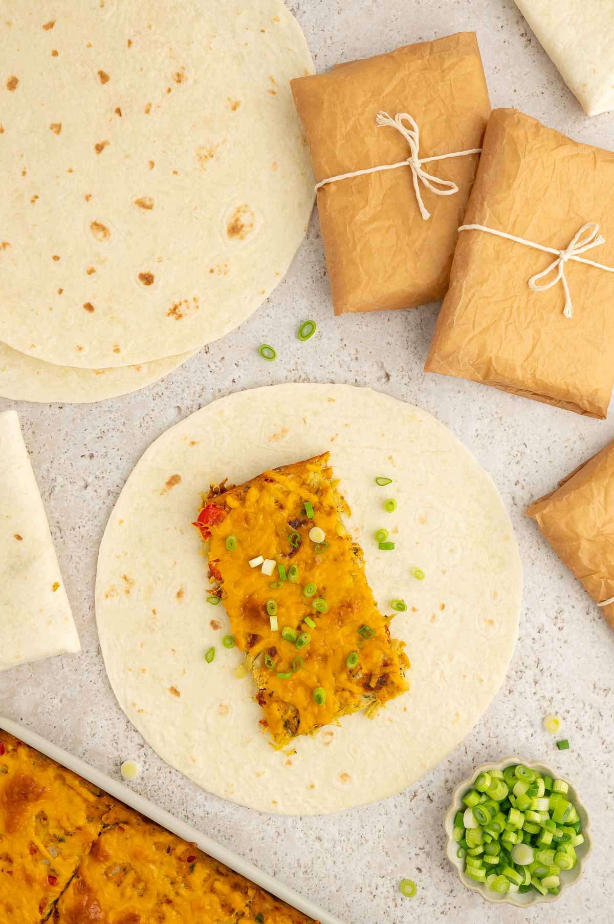 A serving of vegan breakfast burrito filling placed on a large flour tortilla and topped with a sprinkle of sliced green onions.