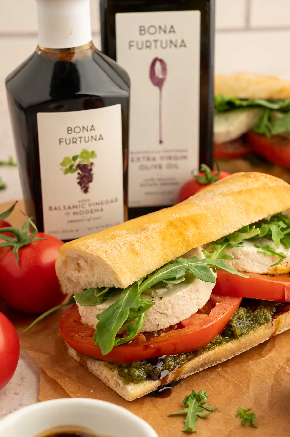 A vegan caprese sandwich next to a bottles of Bona Fortuna's olive oil and balsamic vinegar.