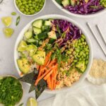Colorful vegan poke bowl with sushi rice, edamame, carrots, avocado, tofu, cucumber, and purple cabbage, topped with spicy mayo and sesame seeds.