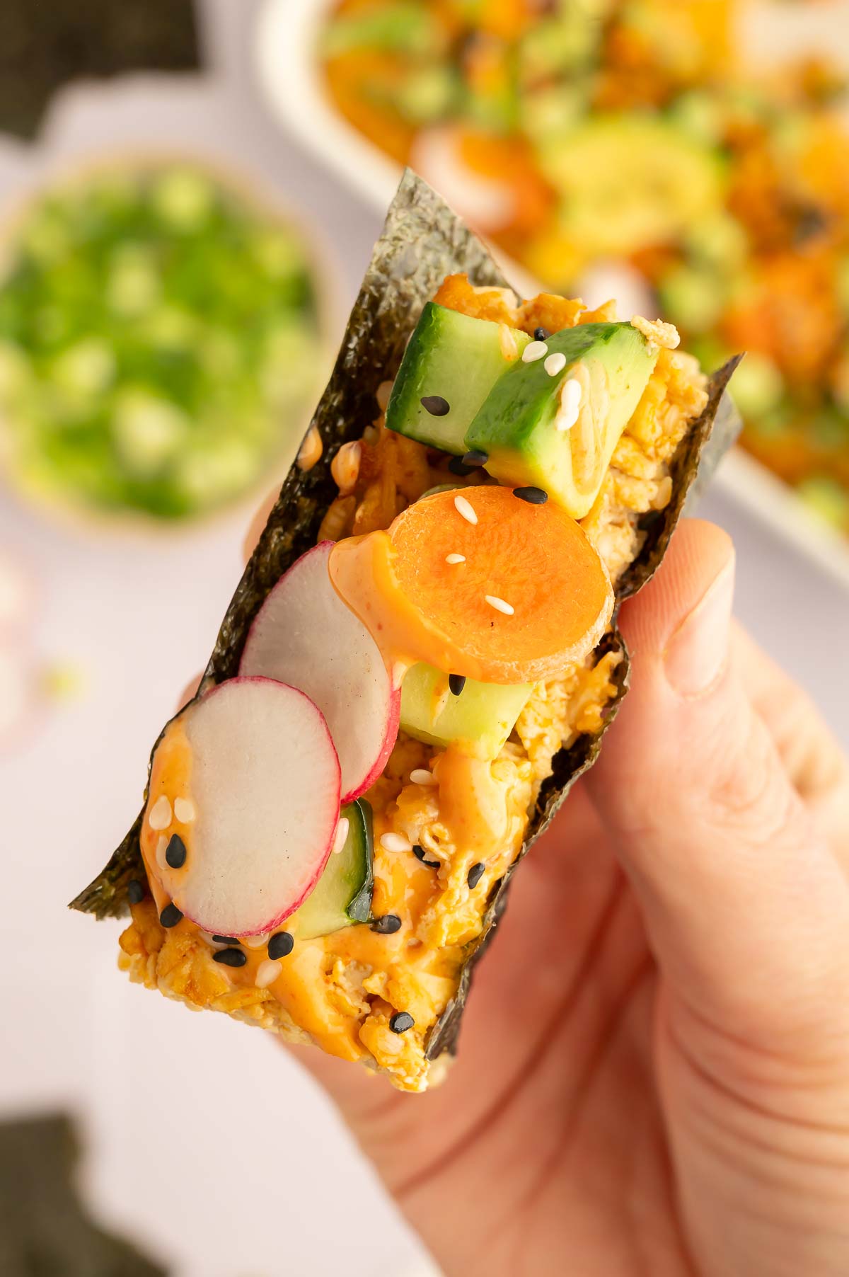 A hand holding a slice of vegan sushi bake that's been wrapped in a piece of nori.