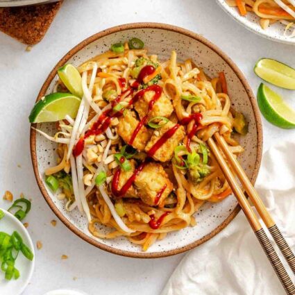Vegan pad Thai bowl with tofu, noodles, lime, and green onion, styled for serving.