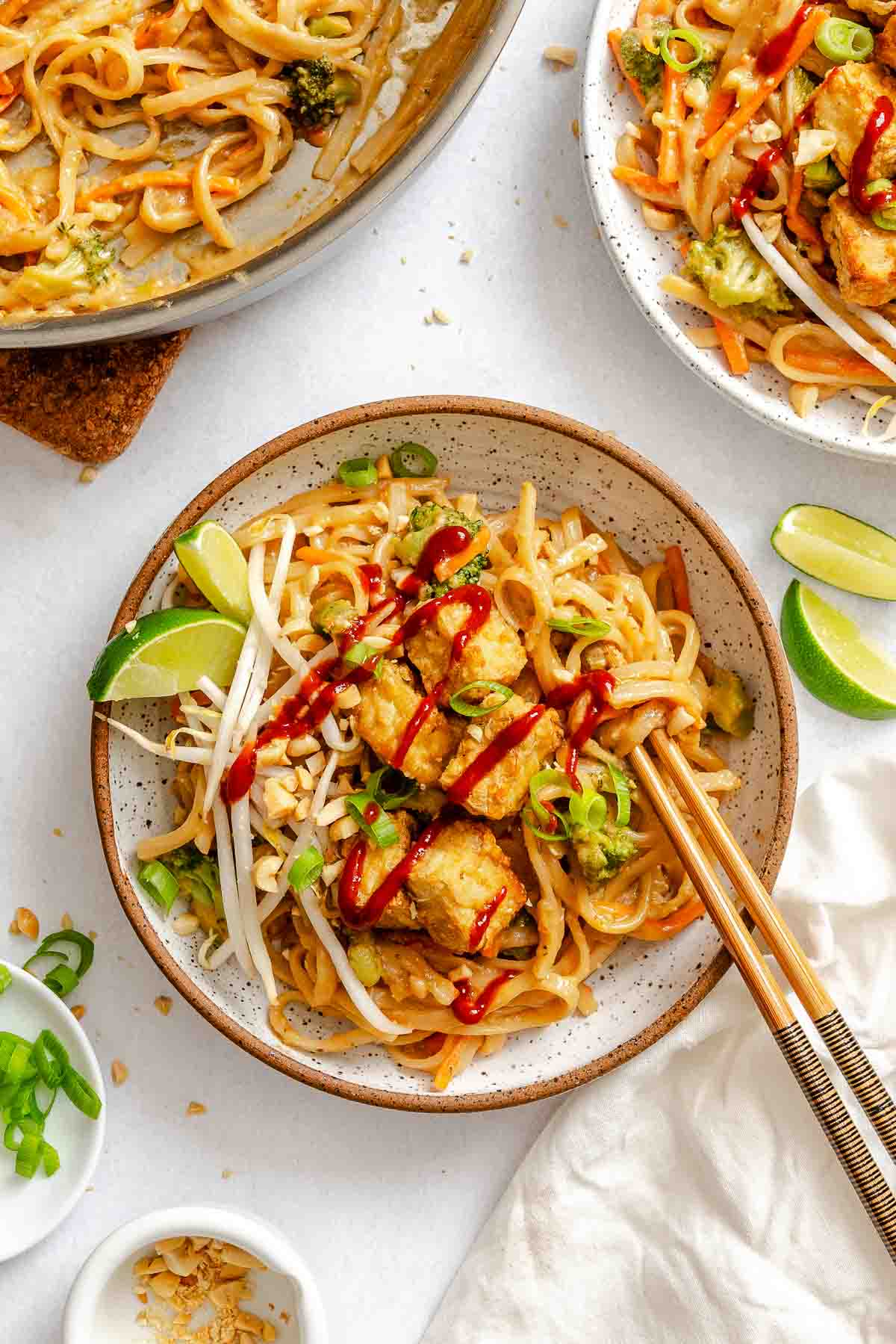 Bowl of vegan pad Thai with crispy tofu, bean sprouts, scallions, and Sriracha drizzle.