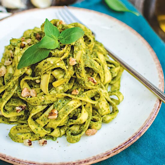 A plate of walnut pesto pasta topped with chopped walnuts and fresh basil leaves.