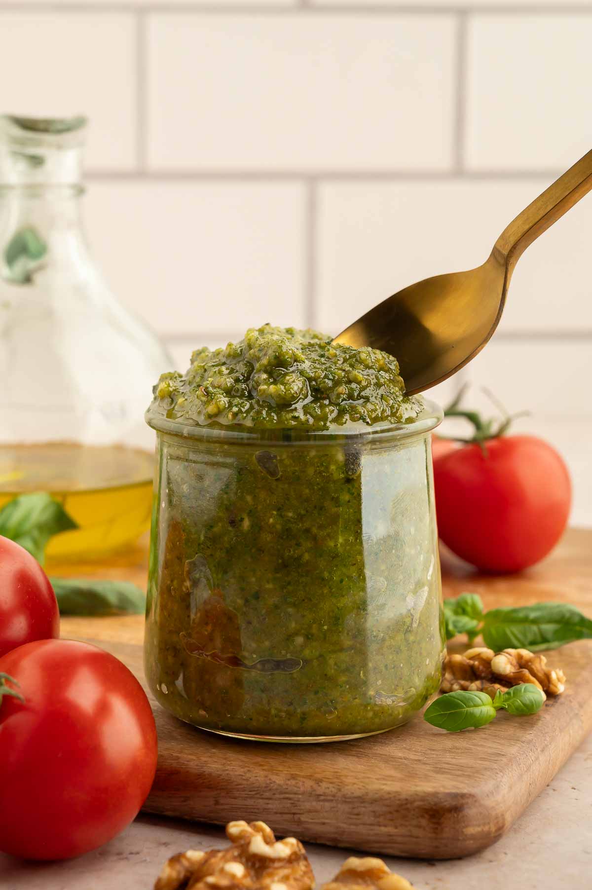 Freshly made walnut pesto in a glass jar with a spoon scooping into it.