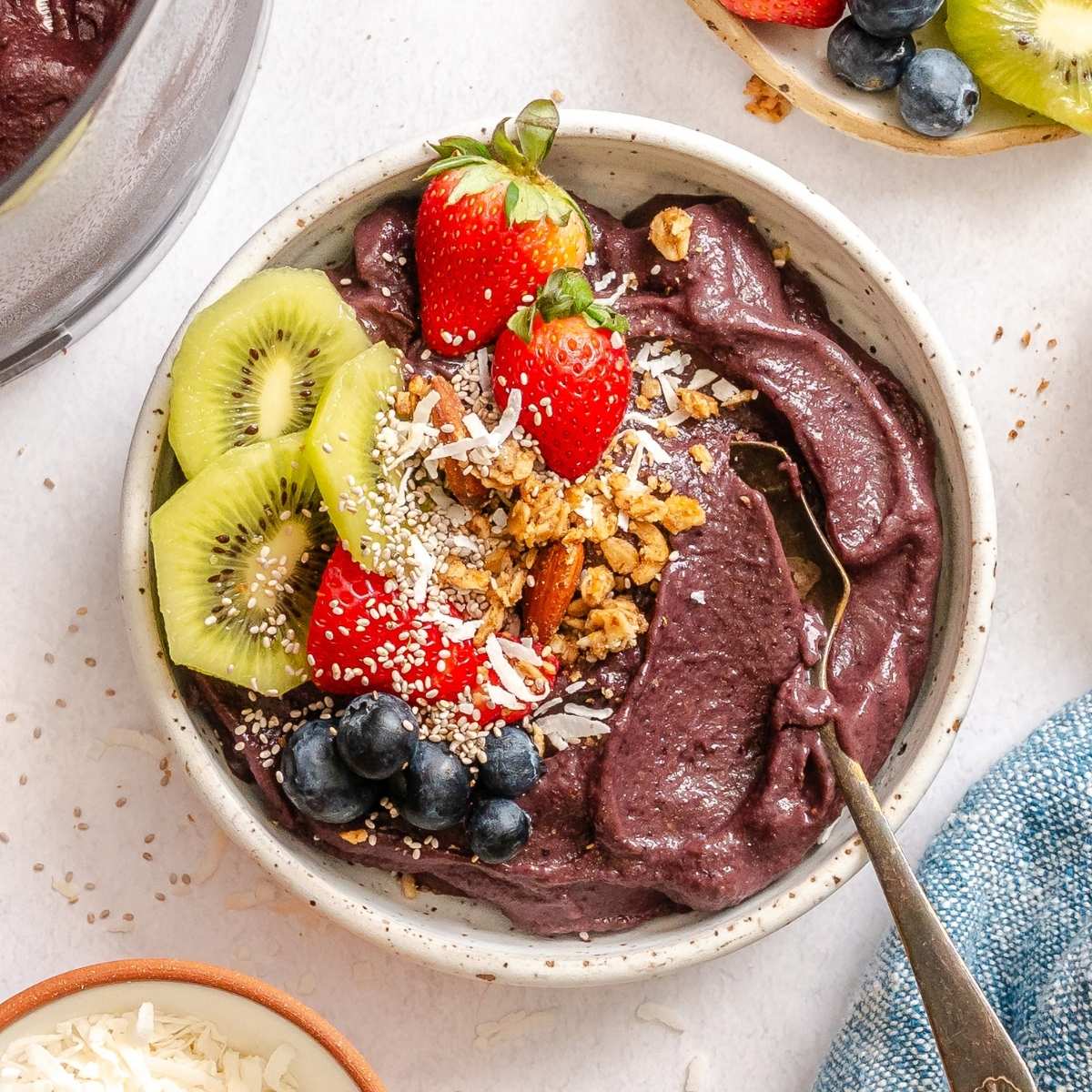 Dairy-free Acai bowl with fresh kiwis, strawberries, blueberries and flaked coconut for garnish in a white bowl with a spoon.