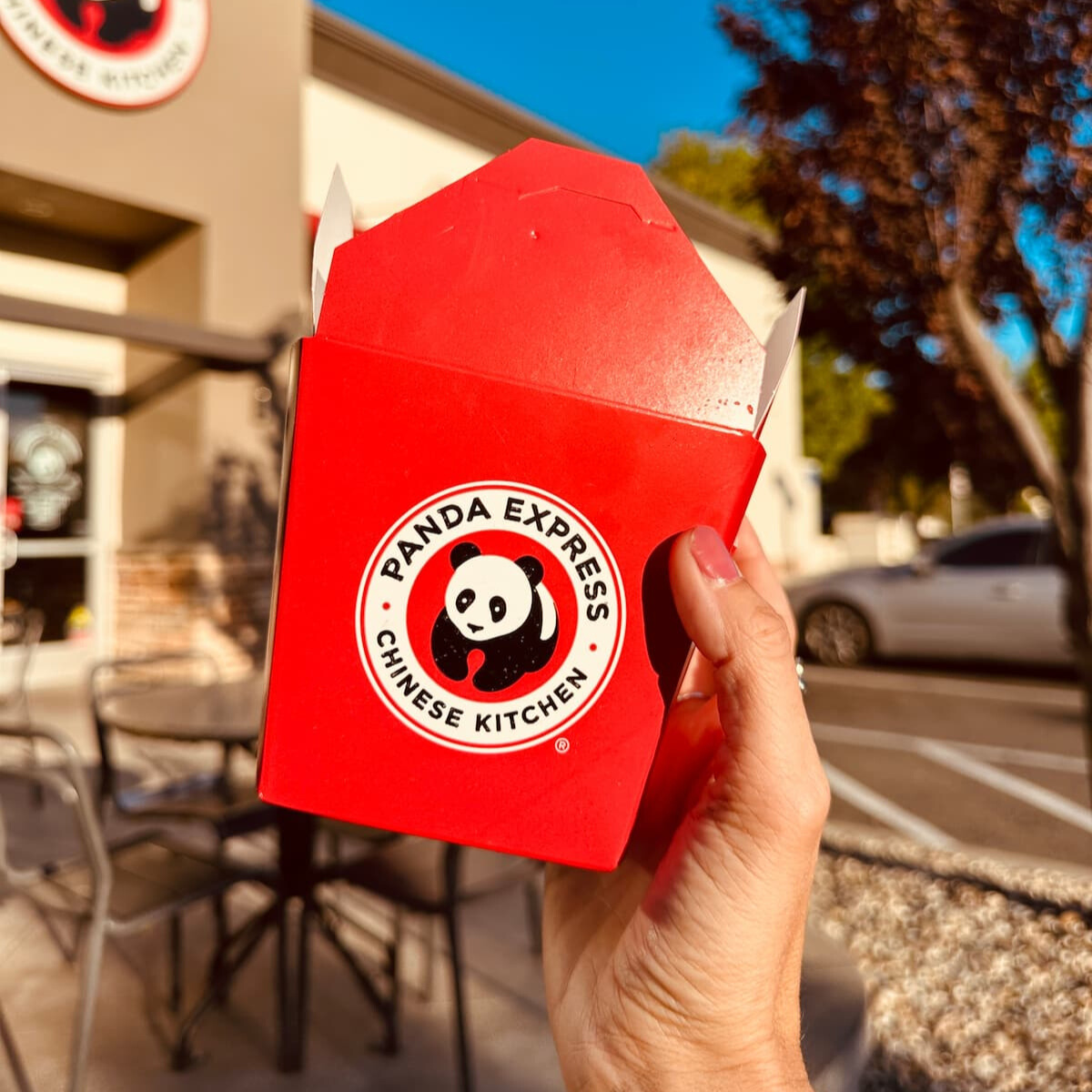 A hand holding a Panda Express take out container in front of the restaurant.