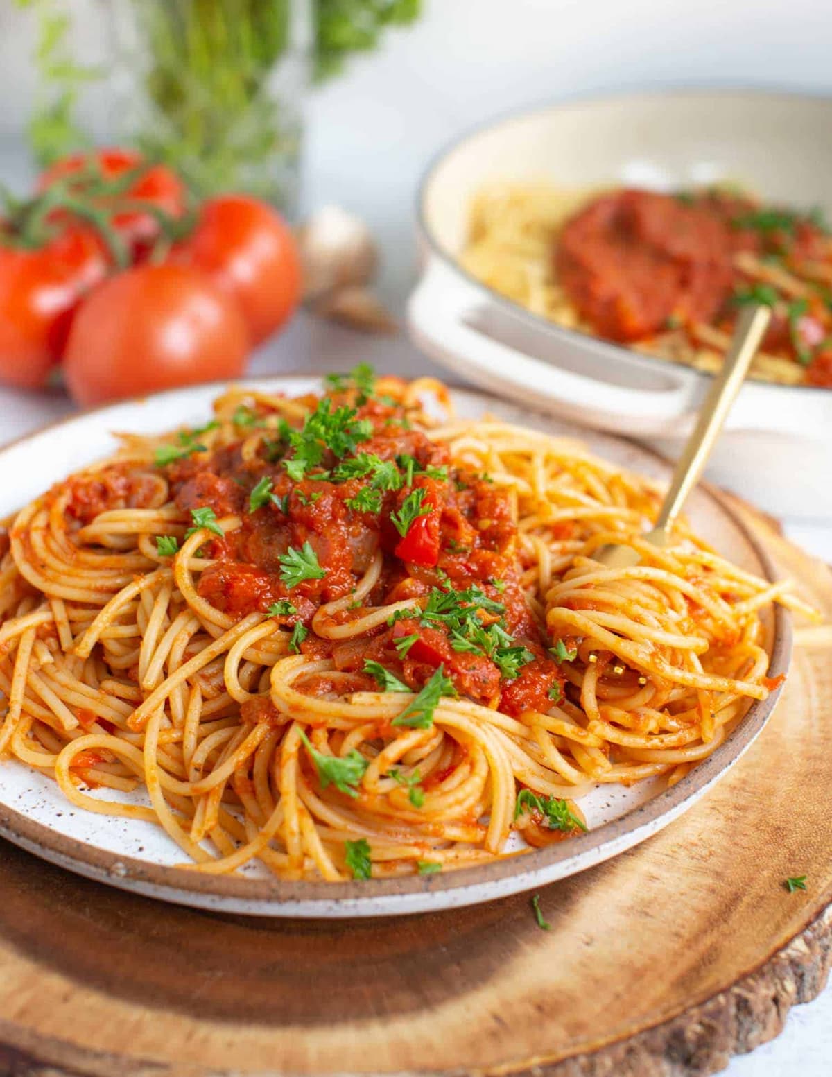 A white dish of vegan spaghetti arrabbiata next to a vine of fresh tomatoes. 