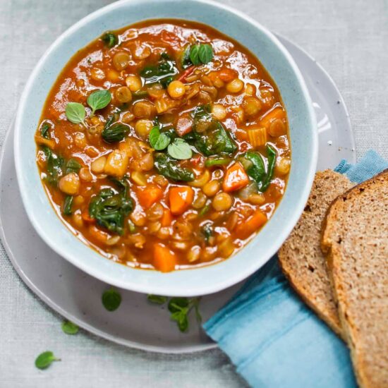 A bowl of vegan slow cooker lentil stew next to a couple of slices of whole grain bread.