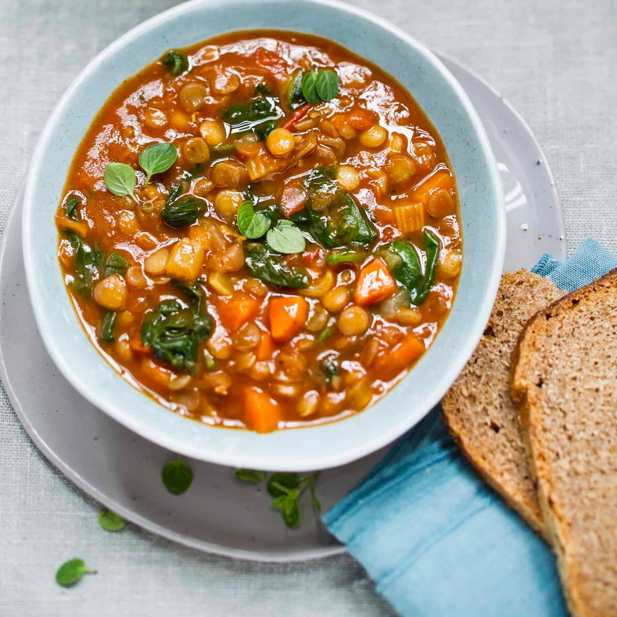 A bowl of vegan slow cooker lentil stew next to a couple of slices of whole grain bread. 