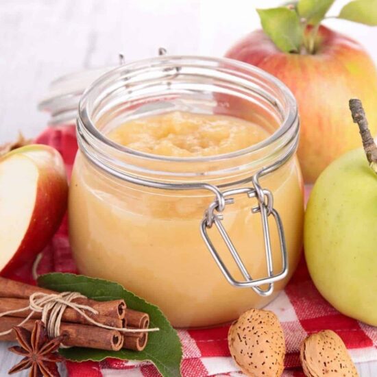 Homemade apple puree (or chunky applesauce) in a mason jar next to cinnamon sticks and green apple.