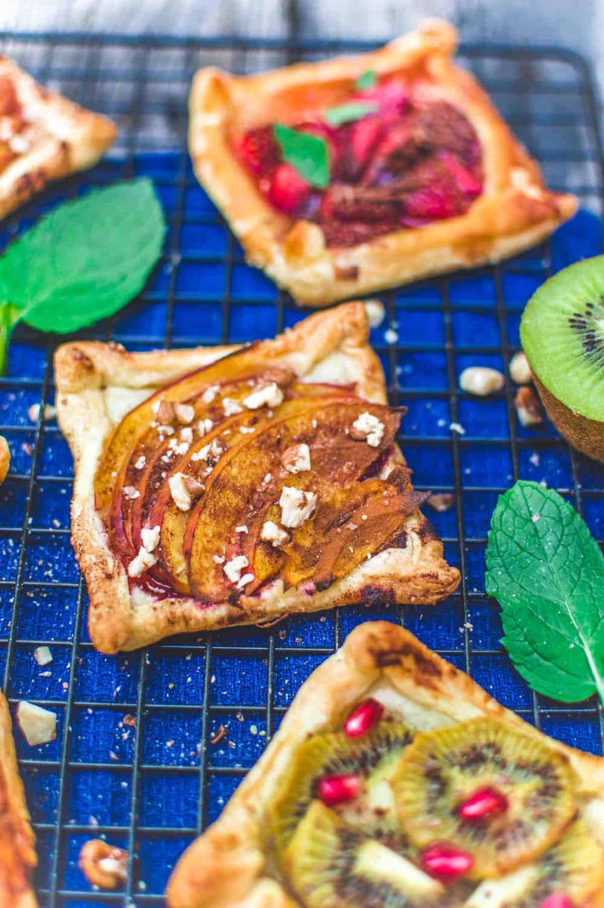A cooling rack with several small pastry vegan fruit tarts and mint leaves.