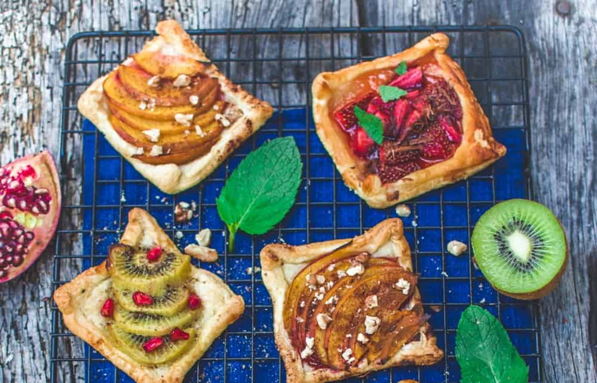 A cooling rack with four mini vegan fruit tarts on it, along with full mint leaves.