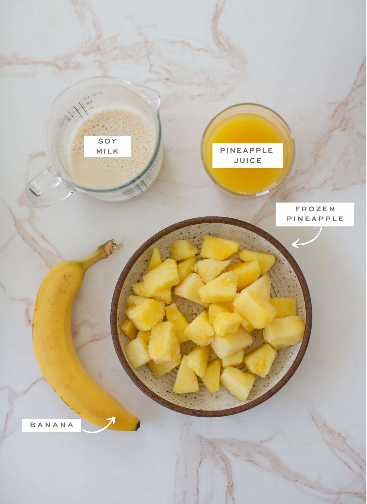 Pineapple banana smoothie ingredients on a marble countertop with labels. 
