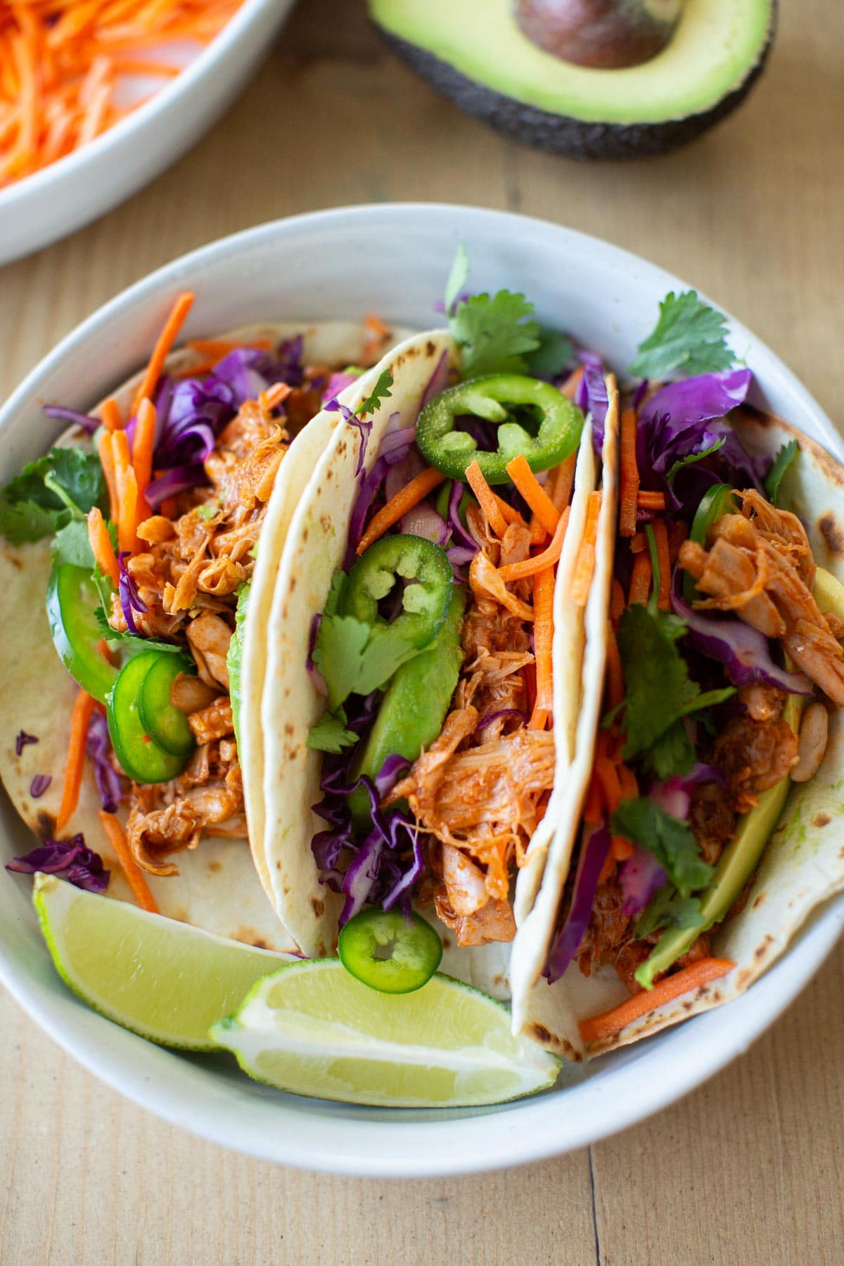 Three vegan jackfruit tacos with bbq sauce in a white bowl garnished with lime wedges and cilantro.
