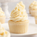A white plate topped with a vegan vanilla cupcake with vegan frosting.