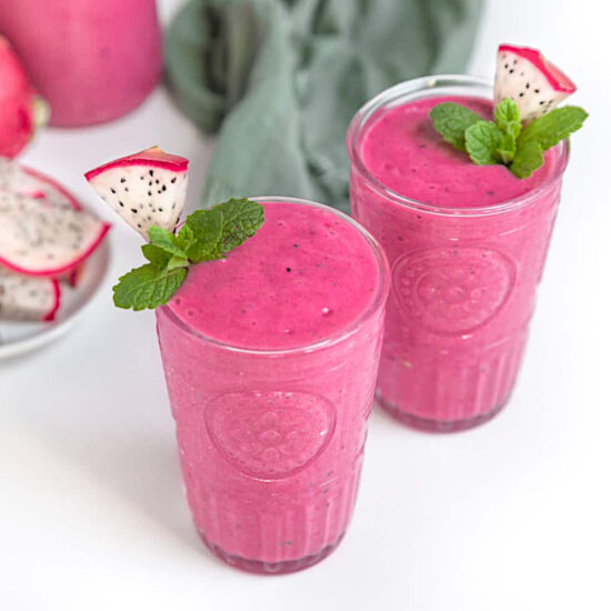 Two pink dragonfruit smoothies in glasses, topped with slices of dragonfruit and mint leaves.