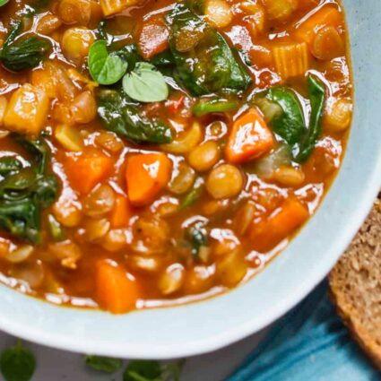 Creamy vegan slow cooker lentil stew with vegetables and homemade bread on the side.