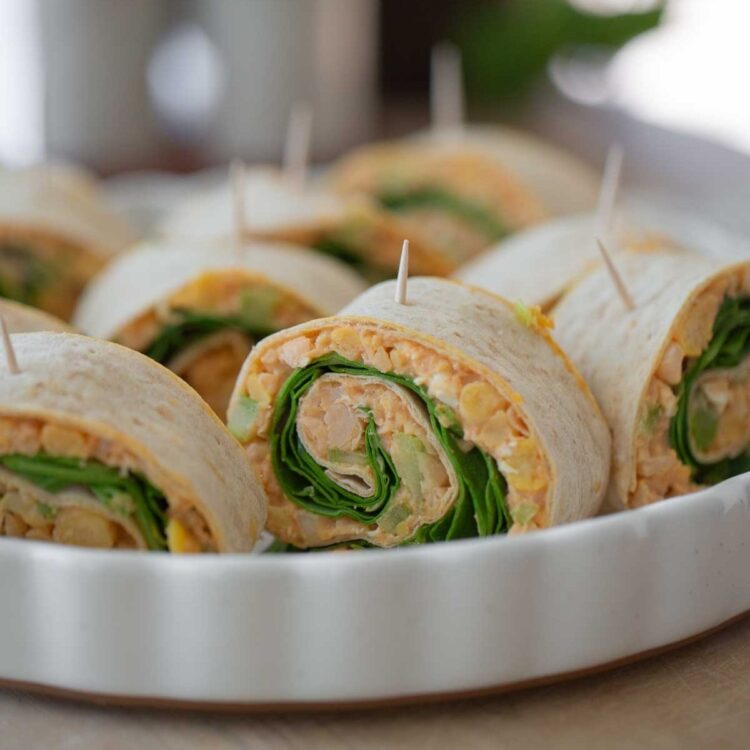Vegan pinwheels with chickpeas, hot sauce and baby spinach served in a white dish as a delicious dairy-free snack or appetizer.
