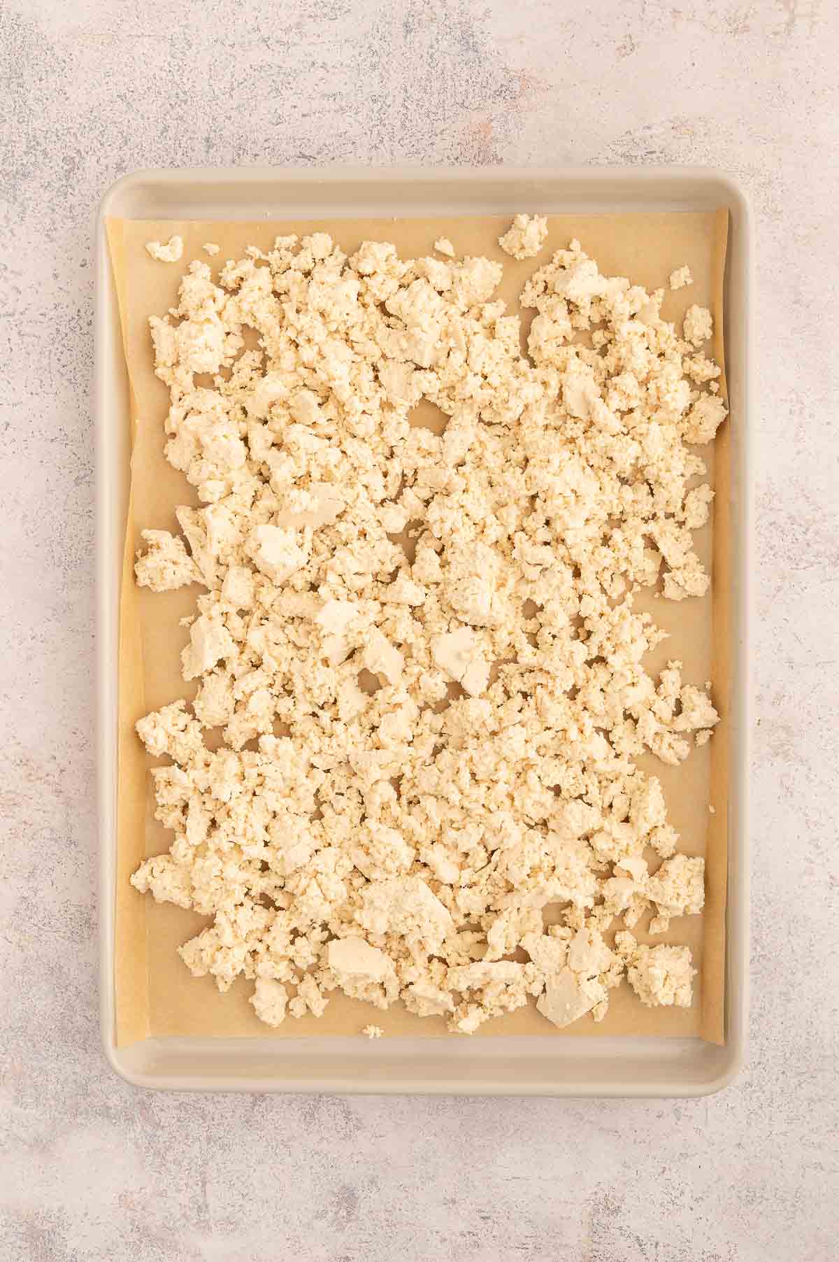 Crumbled tofu spread out on a large baking tray lined with parchment paper.
