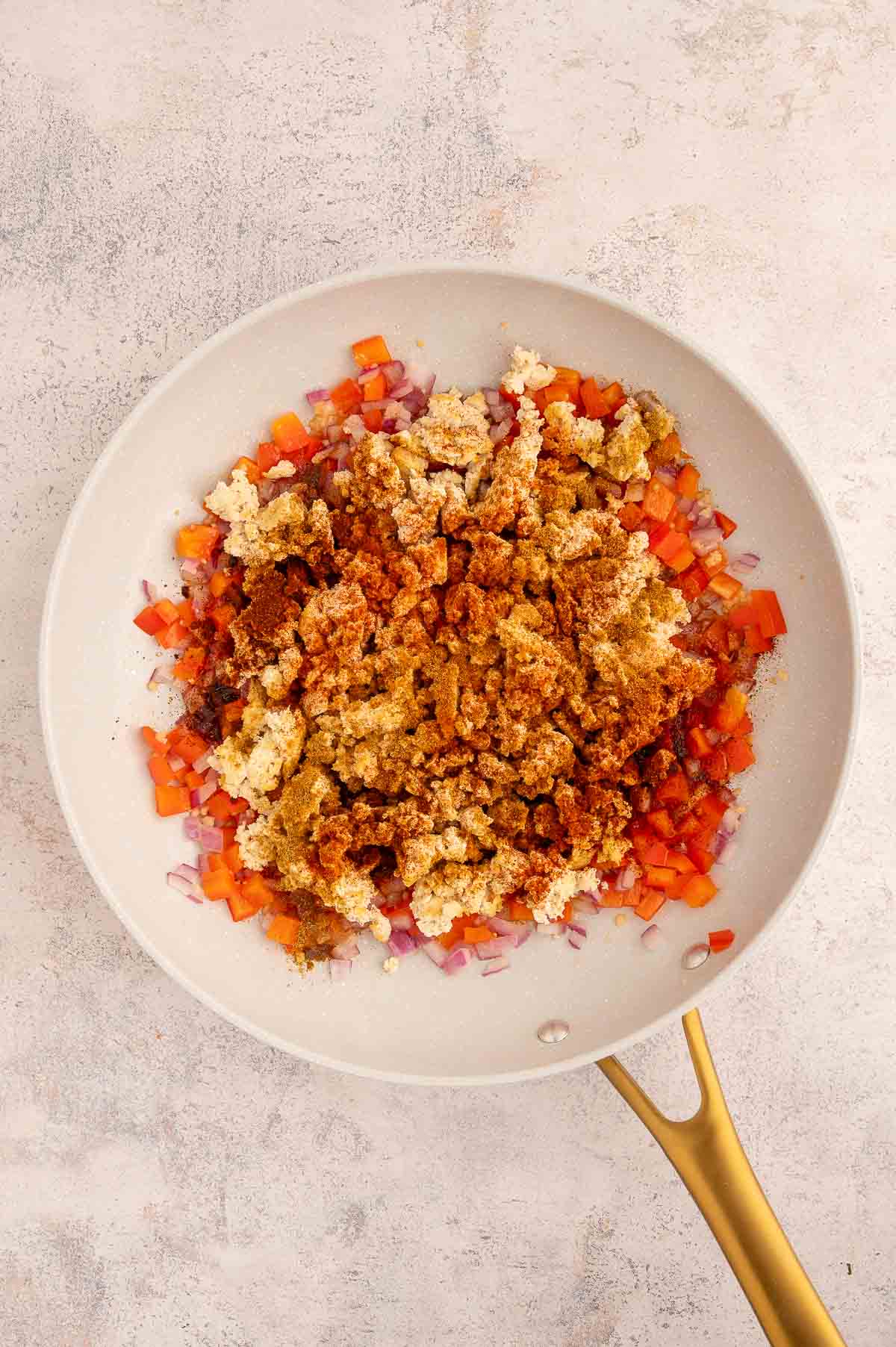Crumbled tofu taco meat added to the saute vegetables with seasonings in a skillet.