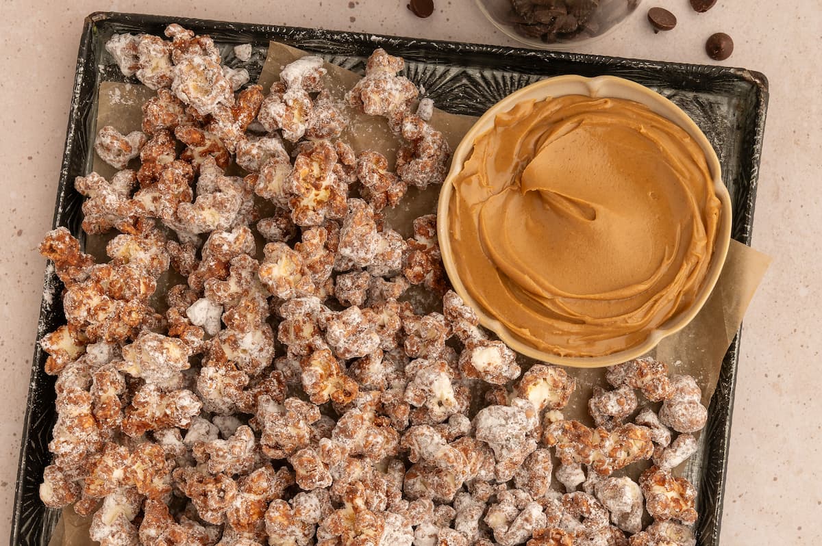 A baking tray full of homemade peanut butter chocolate popcorn and a small bowl of creamy peanut butter on the side.