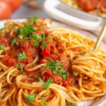Spaghetti Arrabiata recipe on a white plate with a fork swirling a bite and garnished with fresh parsley.