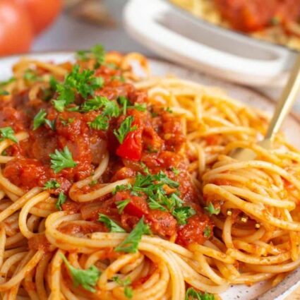 Spaghetti Arrabiata recipe on a white plate with a fork swirling a bite and garnished with fresh parsley.
