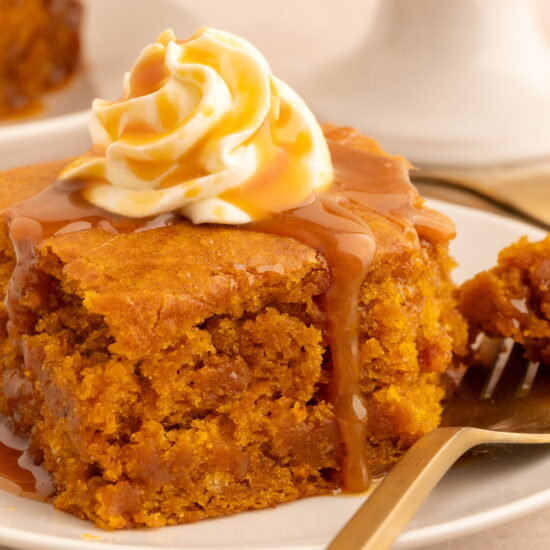 A slice of vegan pumpkin dump cake topped with vegan whipped cream and a drizzle of vegan caramel.