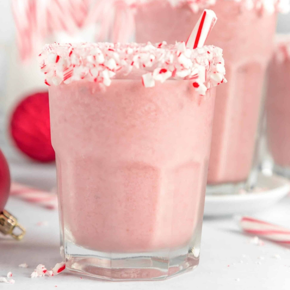 A glass of dairy-free peppermint smoothie with crushed candy canes on the rim and a peppermint stick for stirring.