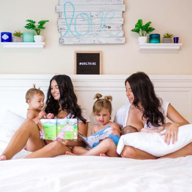 Two moms and their children sitting on a big bed with a white cover under a sign that says "love".