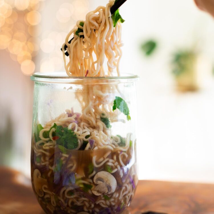 Chopsticks lifting ramen noodles from a jar of meal-prepped ramen.