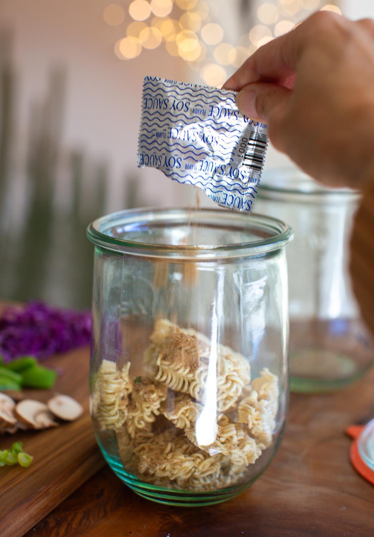 A hand pouring the ramen seasoning over the ramen noodles in a glass jar.