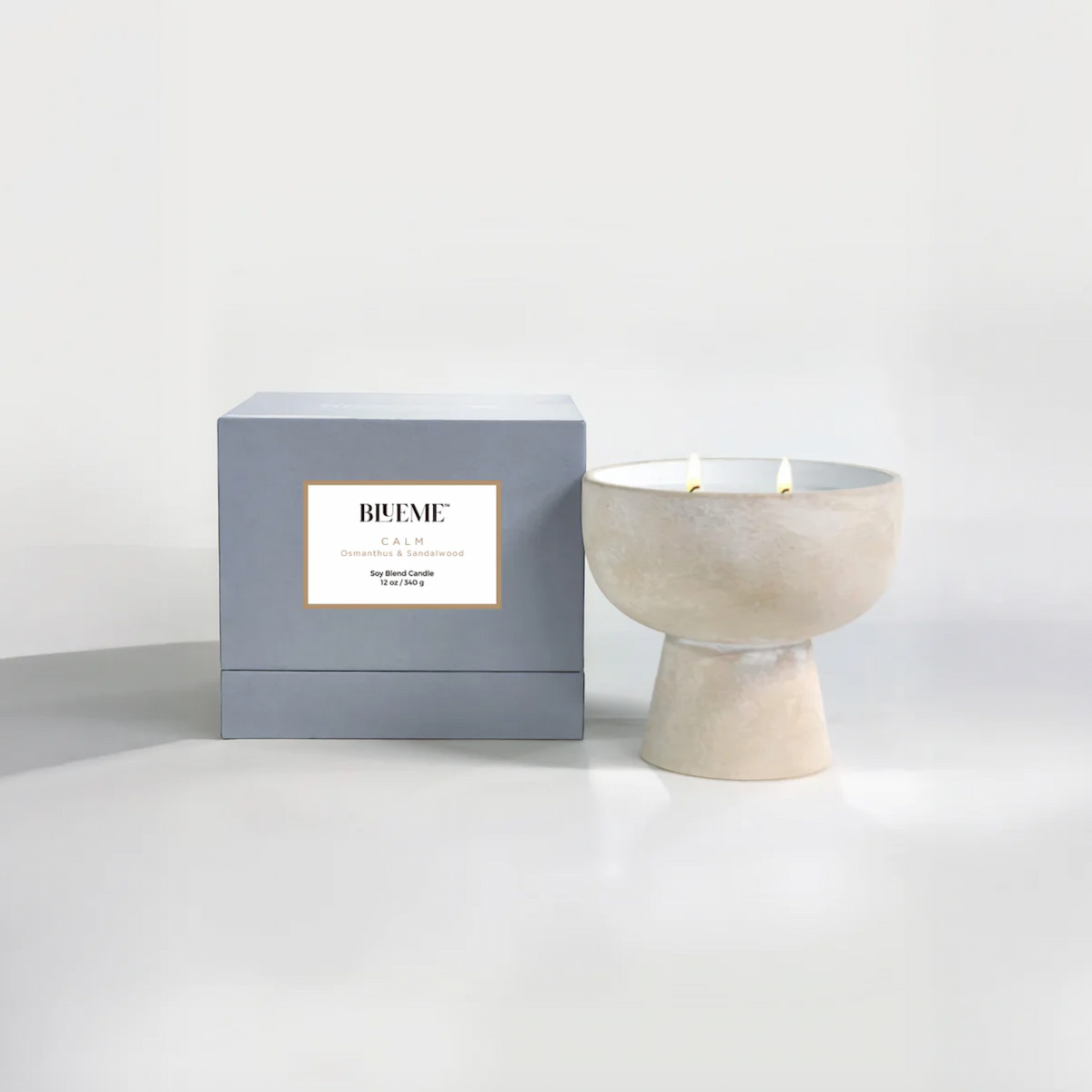 A vegan luxury gift idea of a Blueme Calm candle next to its gray and white box on a white background.