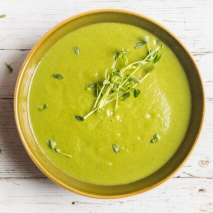 A bowl filled with a healthy green detox soup recipe and garnished with fresh green sprouts.