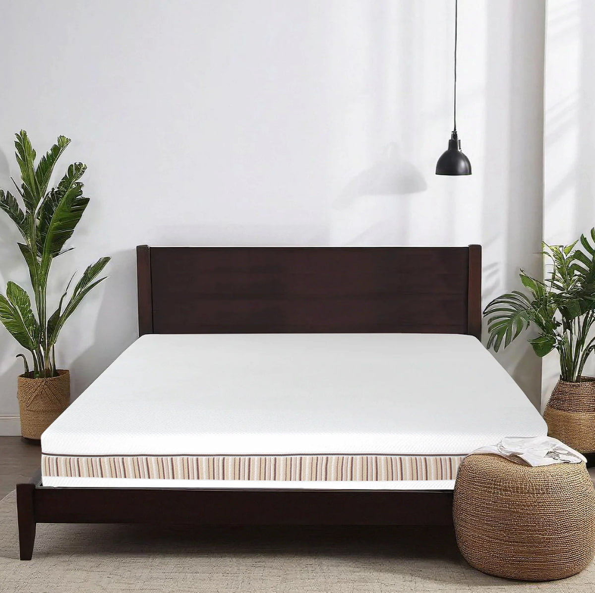 The Essentia vegan mattress on a dark wood bed frame surrounded by tropical plants against a white wall.