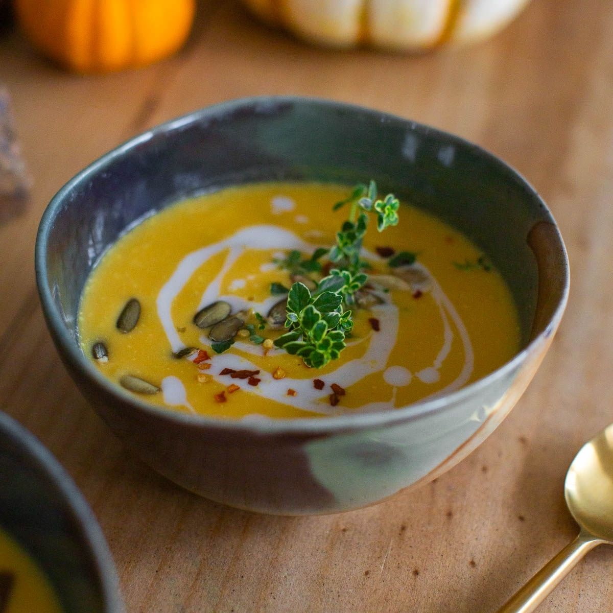 Vegan butternut squash soup garnished with cashew cream and fresh greens next to a gold spoon.