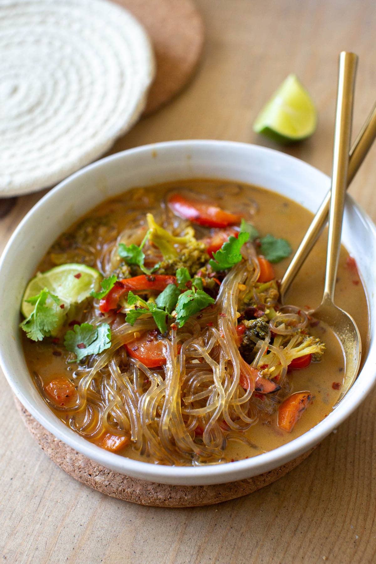 Close up view of vegan glass noodles soup recipe with vegetables in a ceramic bowl with gold utensils.