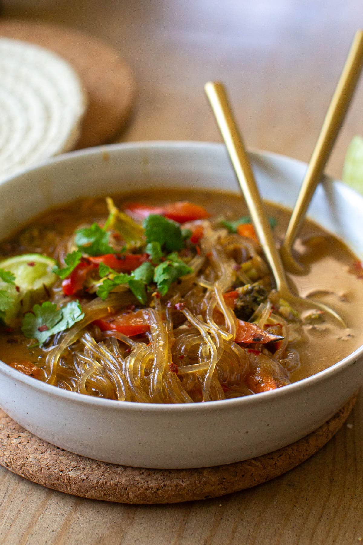 Side view of a ceramic bowl filled with sweet potato glass noodle soup and vegetables and garnished with lime.