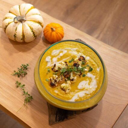 Kabocha squash soup in a glass bowl garnished with fresh sage and next to two pumpkins.