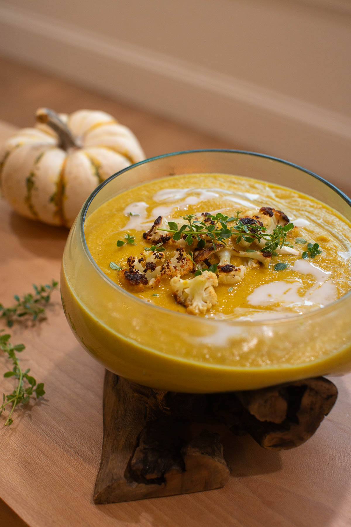 Side view of vegan kabocha squash soup in a glass bowl topped with pieces of roasted cauliflower and next to a white pumpkin.