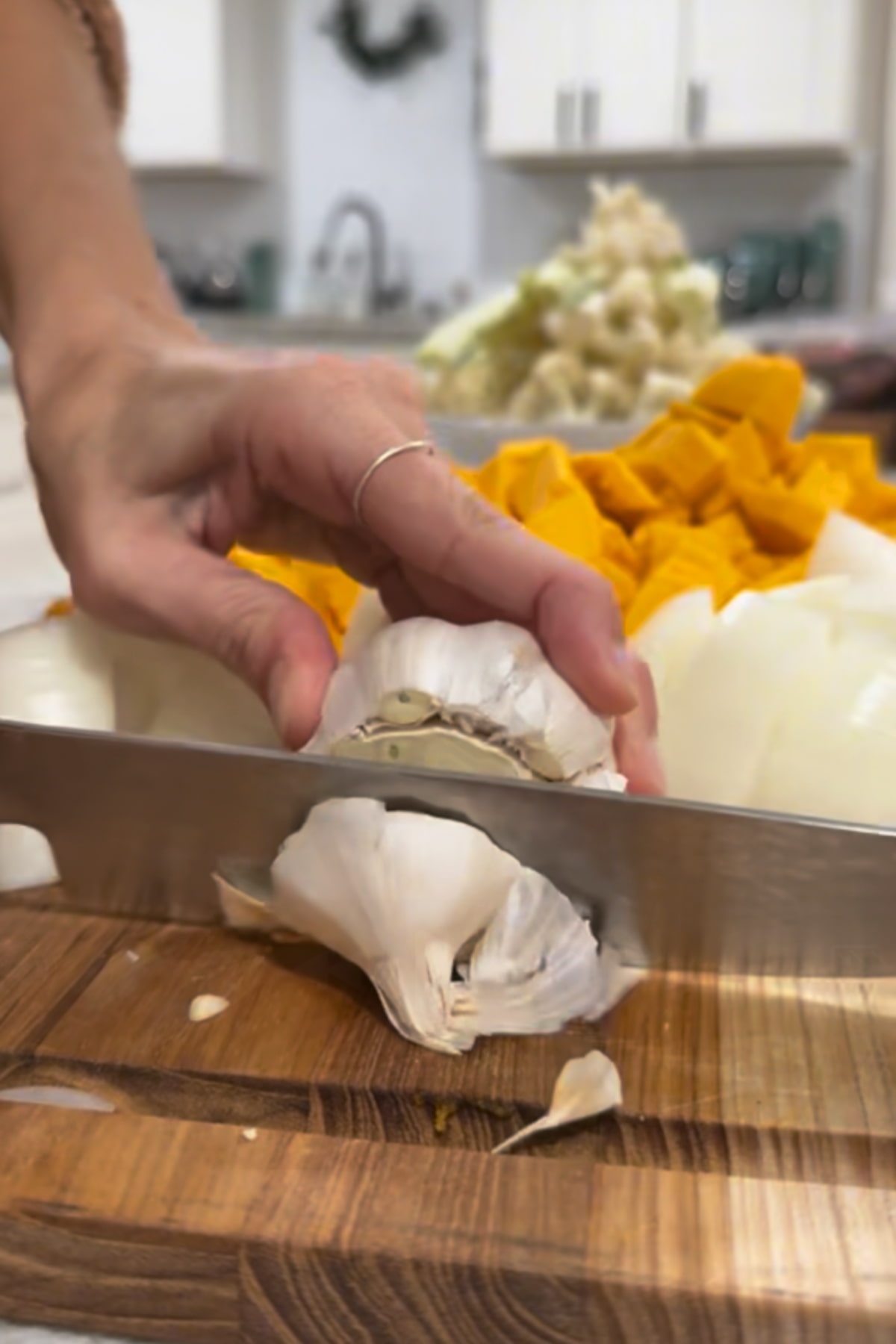A knife is cutting the top off a head of garlic.
